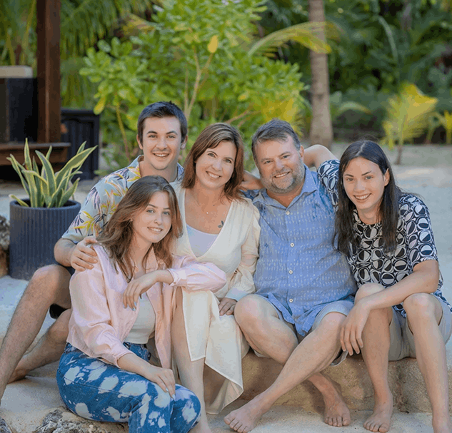 Group of five individuals seated outdoors, surrounded by greenery, conveying a relaxed atmosphere, with a focus on family or friendship connections.